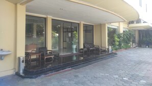 A hotel entrance with a covered outdoor seating area, a trash bin, and a potted plant.