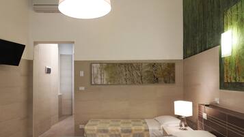 Una camera d'albergo con un letto, un comodino con una lampada, una TV a parete e un quadro.