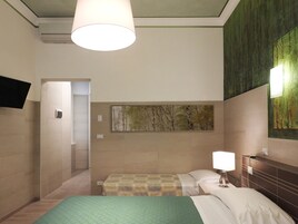 Una camera d'albergo con un letto, un comodino con una lampada, una TV a parete e un quadro.
