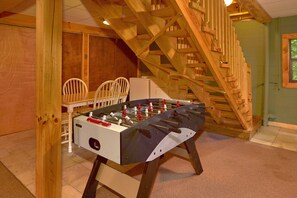 A foosball table in a room with wooden chairs, a staircase, and a green wall.
