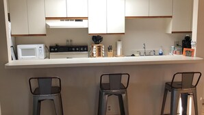 A compact kitchen with a microwave, stove, and sink, featuring a bar area with stools. - Cozy Condo on the water (Dunnellon)