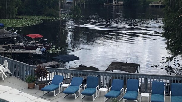 A pool area with lounge chairs and a dock extending into a lake, surrounded by trees. - Cozy Condo on the water (Dunnellon)