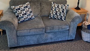 A grey sofa with patterned cushions, a sailboat and fish decoration on the wall, a lamp, and a wicker basket on the floor. - Cozy Condo on the water (Dunnellon)