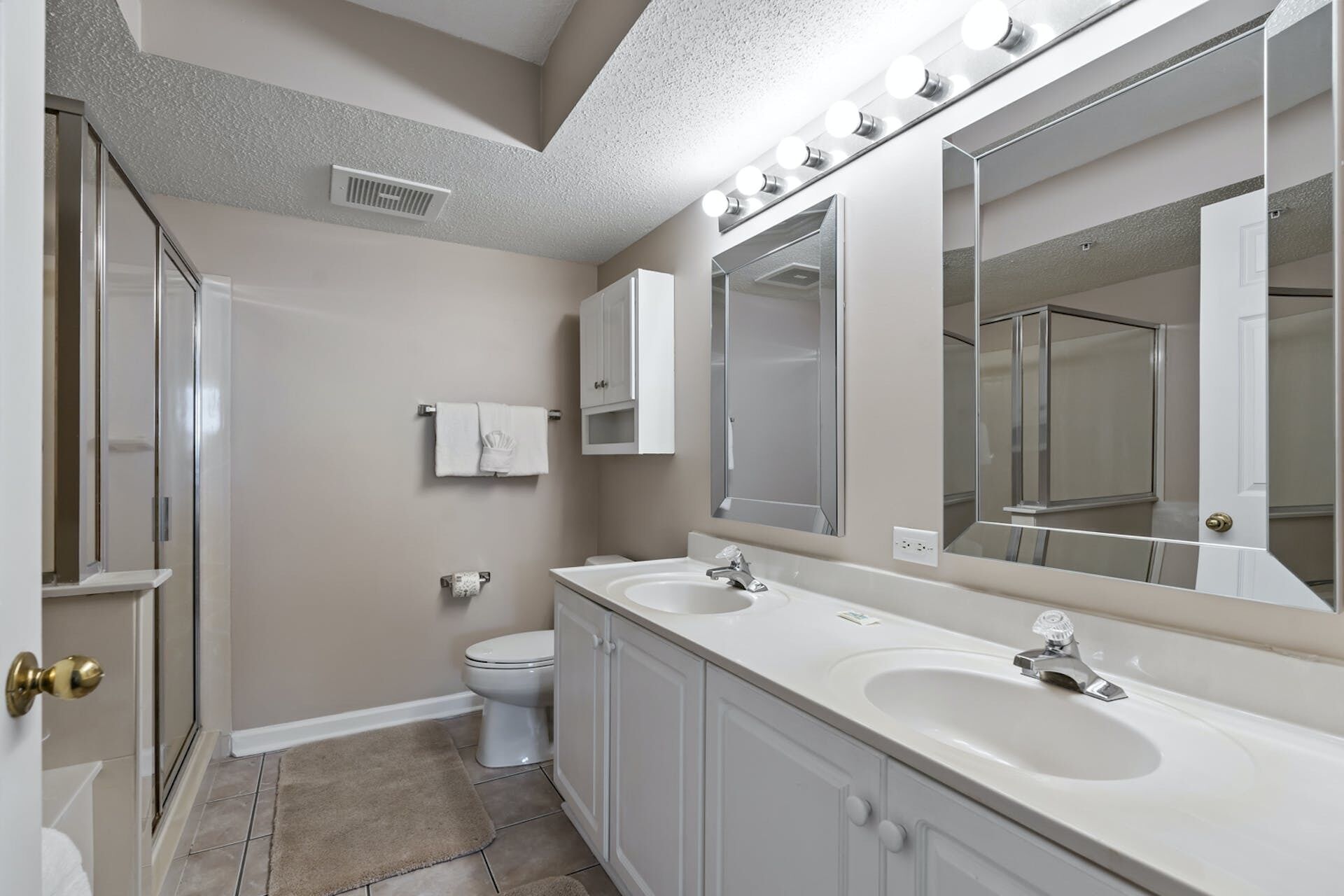 A bathroom with two sinks, a toilet, a towel rack, a mirror, and a shower door.