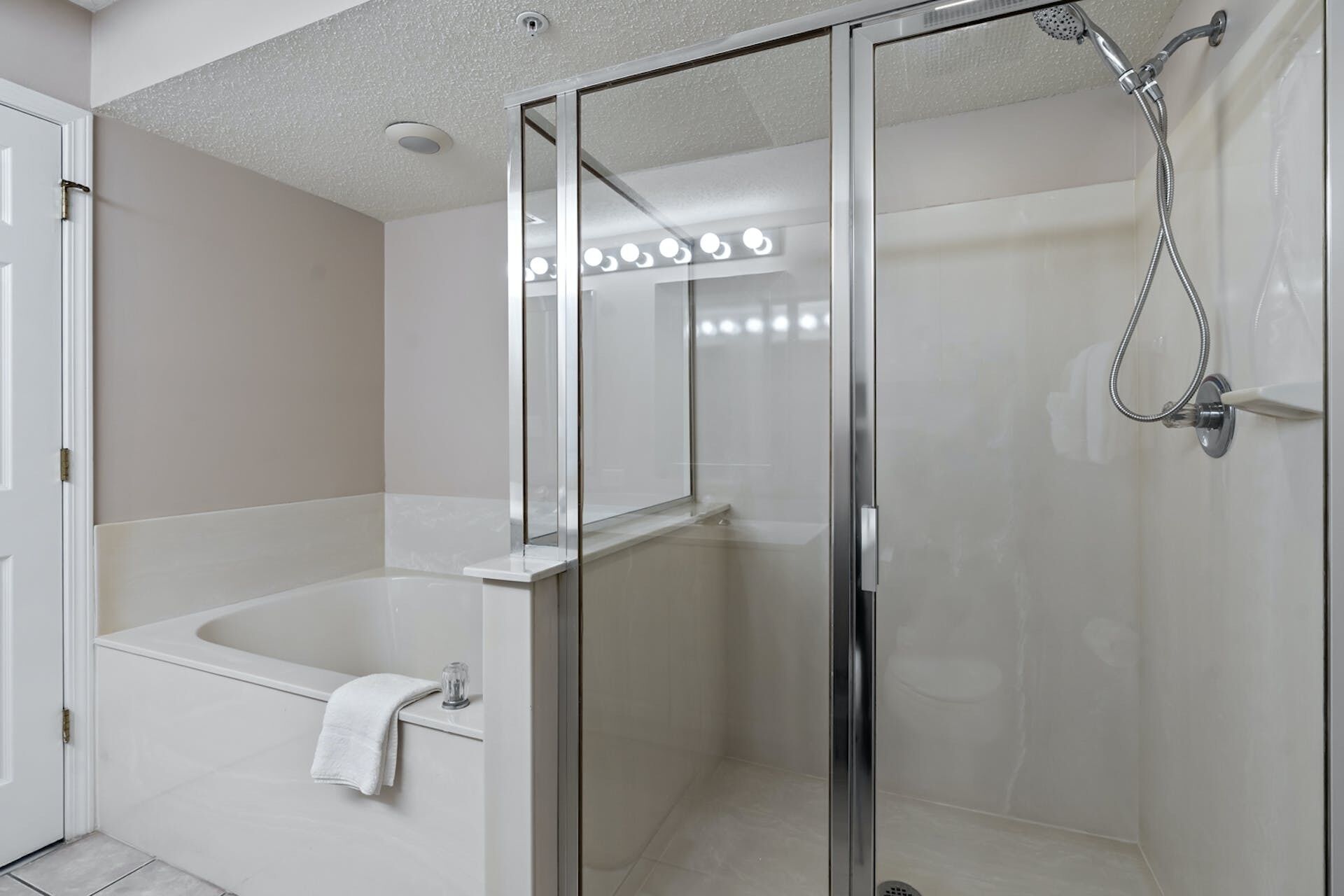 Een moderne badkamer met een douchecabine van glas, een witte badkuip en een glazen douchekop.