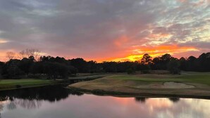 Un parcours de golf avec un étang dans lequel se reflète le ciel au coucher du soleil.
