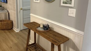 Un couloir avec une console en bois, des œuvres d’art encadrées, un miroir rond et un téléviseur fixé au mur.