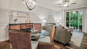 Un salon avec une table basse en verre, des fauteuils en osier, un canapé gris et un ventilateur de plafond.