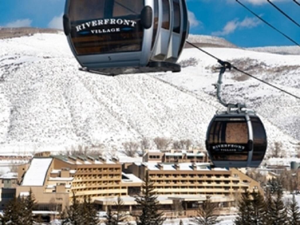 A cable car with 'Riverfront Village' written on it, a building with multiple floors, and a snowy mountain in the background.