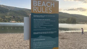 A beach rules sign with information on swimming hours, prohibited activities, lightning guidelines, and available restrooms.