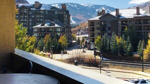 A view of a mountain resort with multiple buildings, a clear sky, and a snow-capped mountain in the background.