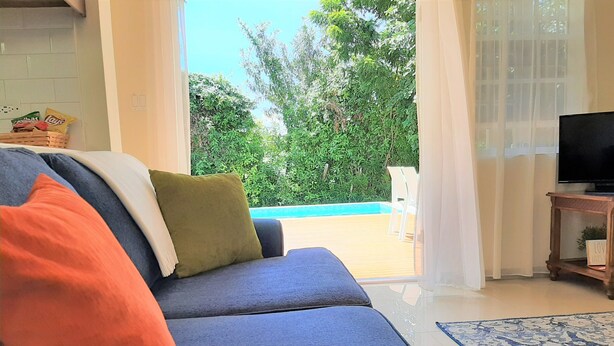 A living room with a sofa, a television, and a view of a pool and greenery. - Sugar Fields Hoilday Home with Private Pool. (Valley Church)