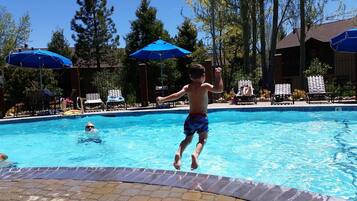 A swimming pool with a child jumping into the water, surrounded by lounge chairs and umbrellas.