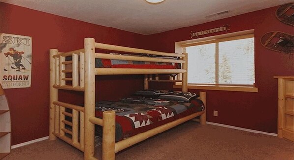 A bunk bed in a room with red walls, a window with a view of trees, and a poster on the wall.