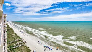 Ein Strand mit einer weiten Sandfläche, einigen Sonnenschirmen und einem Gebäude mit Balkonen mit Blick auf den Strand.