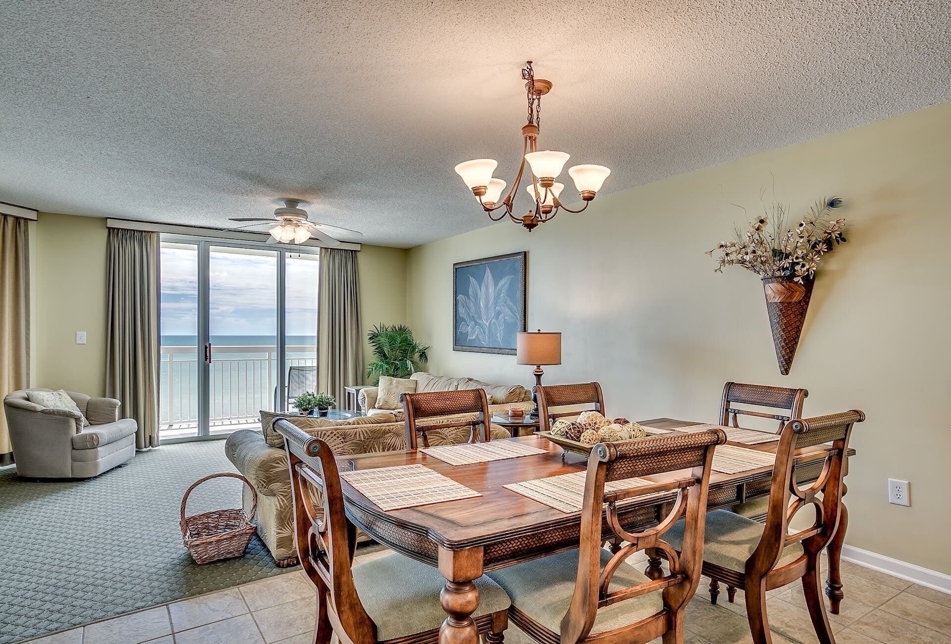 A spacious living room with a dining area, a ceiling fan, and a large window overlooking the ocean.