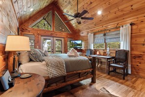 A cozy cabin interior with a bed, a table, a chair, and a television.