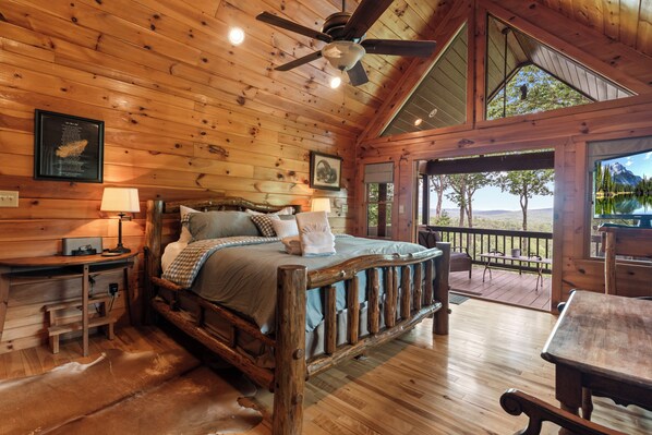 A wooden cabin interior with a bed, a desk, and a view of the outdoors.