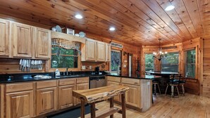 Ein Interieur einer Holzhütte mit einer Küchenzeile, die Holzschränke, eine zentrale Kochinsel und einen Esstisch mit Stühlen umfasst.