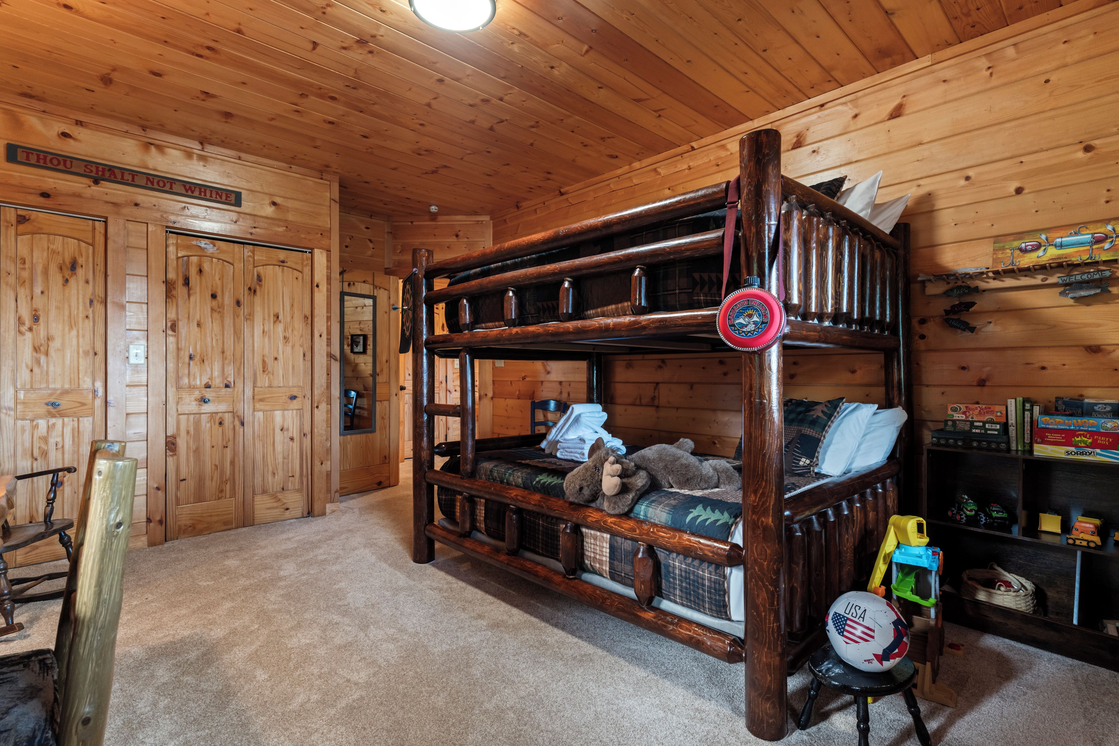 A bunk bed with a wooden headboard, a small table with a teddy bear, and a shelf with various items including a welcome sign and a fish decoration.