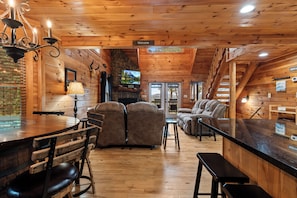 A cozy cabin interior with a stone fireplace, wooden walls, a bar area, and seating. - Drink Up The View - Morganton (Morganton)