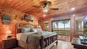 A wooden cabin bedroom with a bed, nightstands, a lamp, and a view of the outdoors. - Drink Up The View - Morganton (Morganton)