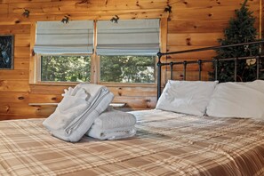 A wooden cabin bedroom with a bed, pillows, and a window.