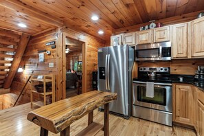A log cabin-style kitchen with wooden walls, a stainless steel refrigerator, a microwave, an oven, and a wooden bench.