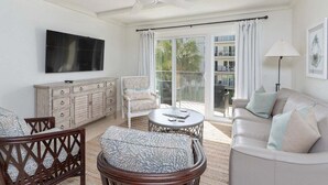 Ein geräumiges Wohnzimmer mit Deckenventilator, einem Flachbildfernseher, einer Couch, einem Couchtisch und einem Essbereich mit Stuhl und Schrank.