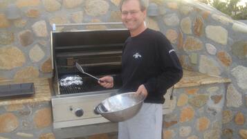A person standing next to a stone-built outdoor grill with a metal bowl and spatula.