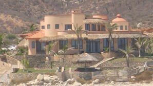 A coastal property with a large house featuring multiple windows, a thatched roof, and a stone wall. - McGann Estate Resort: Two Houses on the Beach, sleeps 14 (Los Barriles)