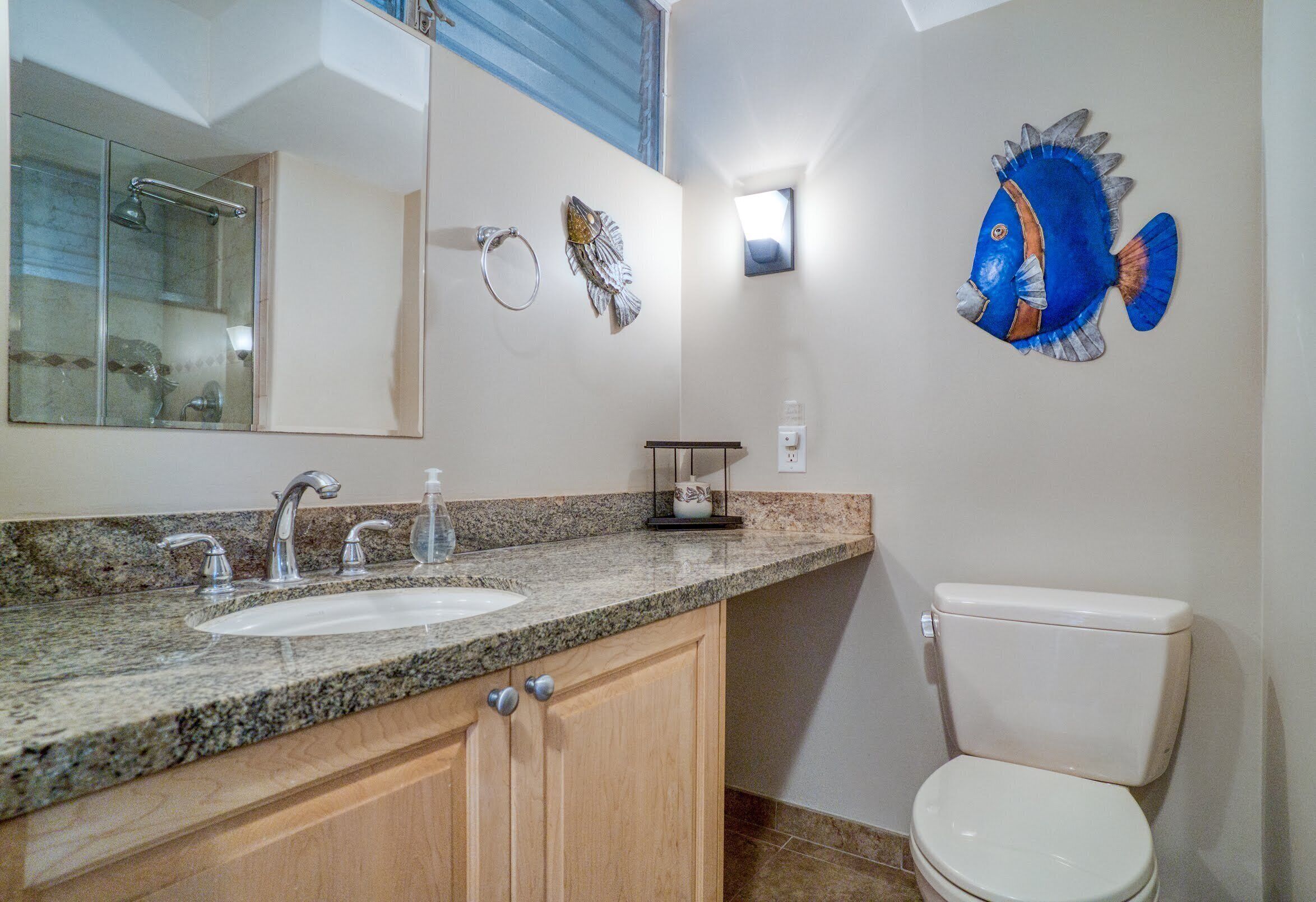 A bathroom with two sinks, a toilet, a mirror, and a decorative fish wall art.
