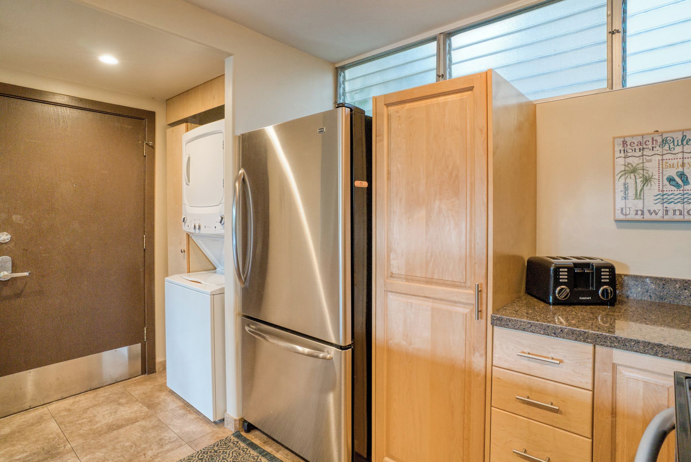 A compact kitchen with a stainless steel refrigerator, a washing machine, wooden cabinets, and a toaster.