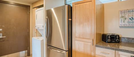 A compact kitchen with a stainless steel refrigerator, a washing machine, wooden cabinets, and a toaster.