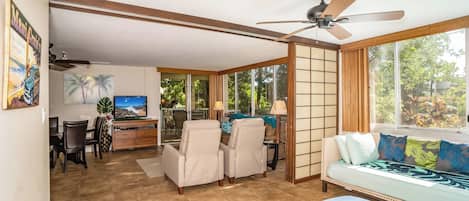 A spacious living area with a large window, a ceiling fan, and a sofa with patterned cushions.
