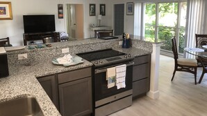 Una cocina moderna con encimeras de granito, horno empotrado y comedor con mesa y sillas de vidrio.