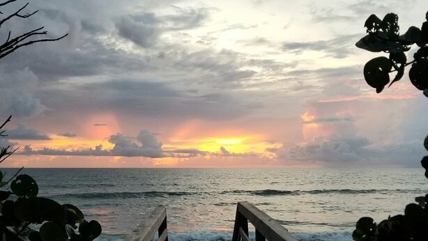Un muelle de madera que conduce a una playa con un atardecer al fondo.