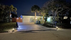 Un camino de entrada lleva a un garaje con una valla de madera a la izquierda y una entrada de casa bien iluminada.
