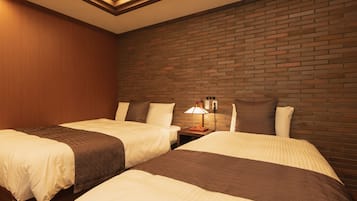 A hotel room with two beds, a brick wall, and a nightstand with a lamp.