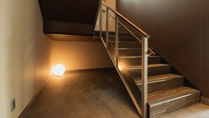 A staircase with a wooden finish and metal handrail, leading to a landing with a light fixture. - GRAND BASE Beppu (Beppu)