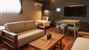 A modern living room with a sofa, coffee table, and dining table. A flat-screen TV is mounted on the wall, and an air conditioning unit is visible. - GRAND BASE Beppu (Beppu)