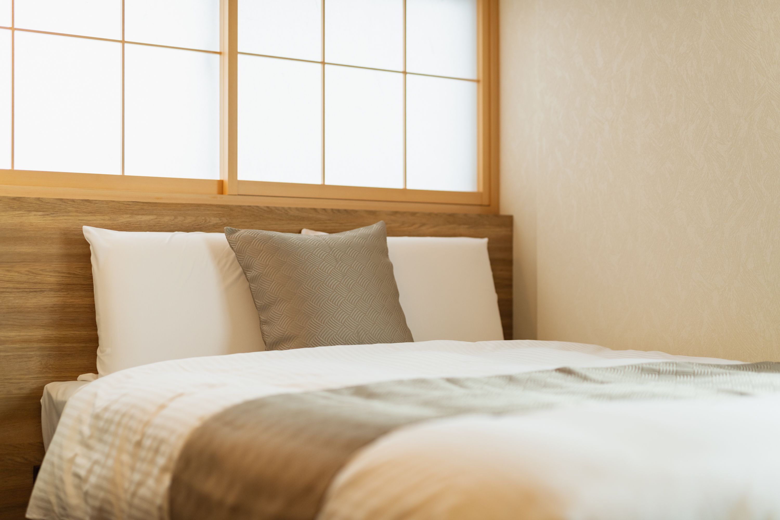 A neatly made bed with a wooden headboard, white and gray pillows, and a light-colored blanket.