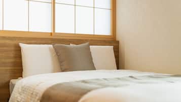 Una cama bien tendida con cabecera de madera, almohadas blancas y grises, y una manta de color claro.