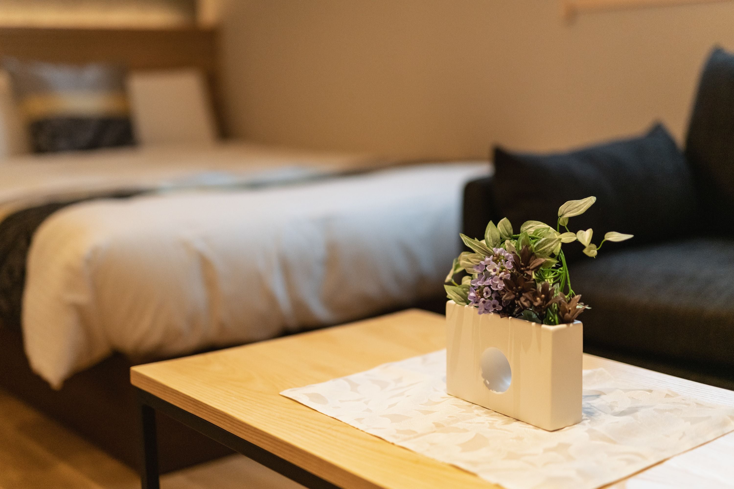 A neatly arranged room with a bed, a small table with a plant, and a sofa with cushions.