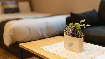 A neatly arranged room with a bed, a small table with a plant, and a sofa with cushions.