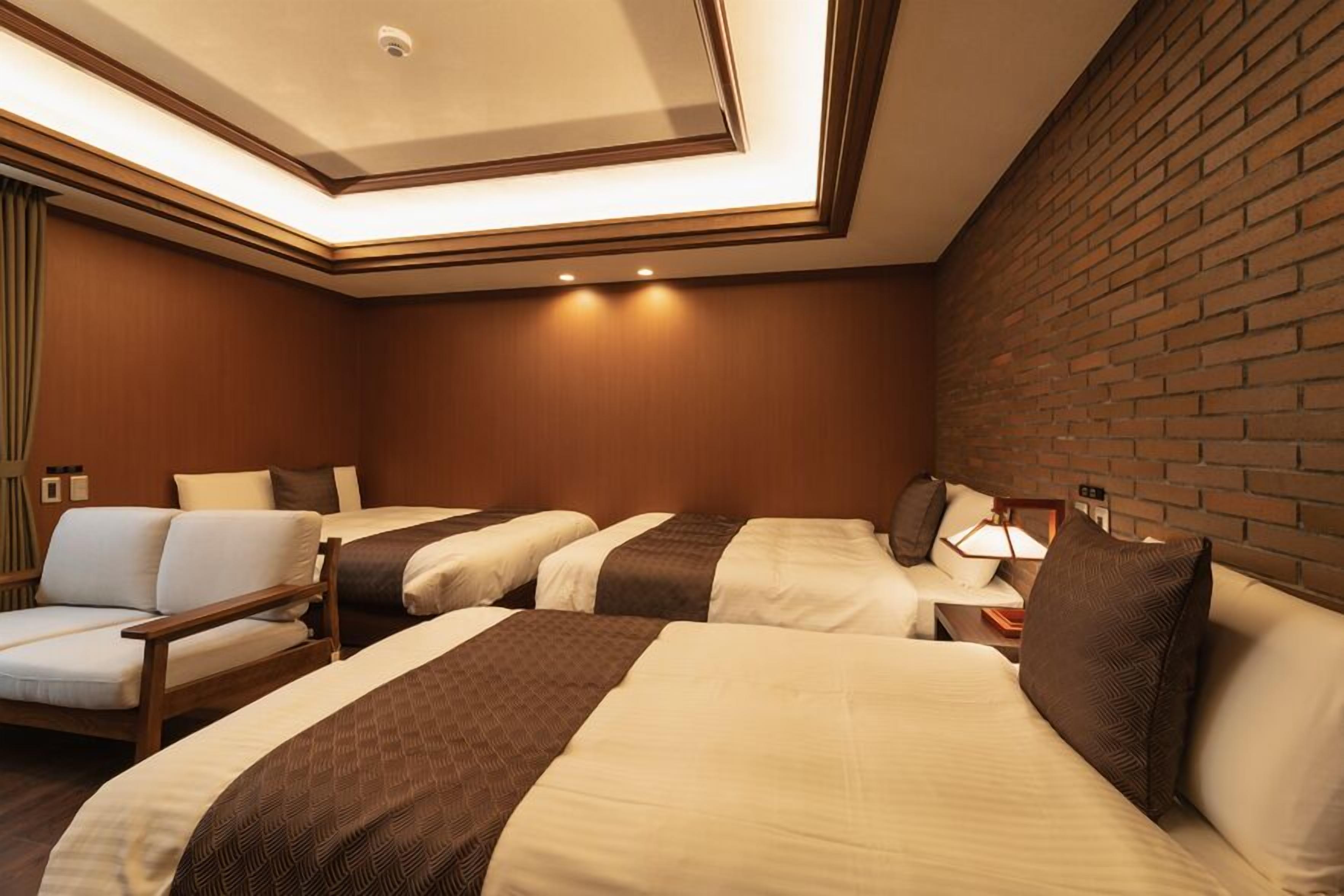 A hotel room with three beds, a sofa, and a brick wall.