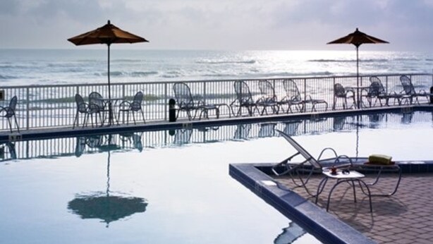 Une piscine à débordement avec vue sur l’océan, deux parasols et des chaises longues.