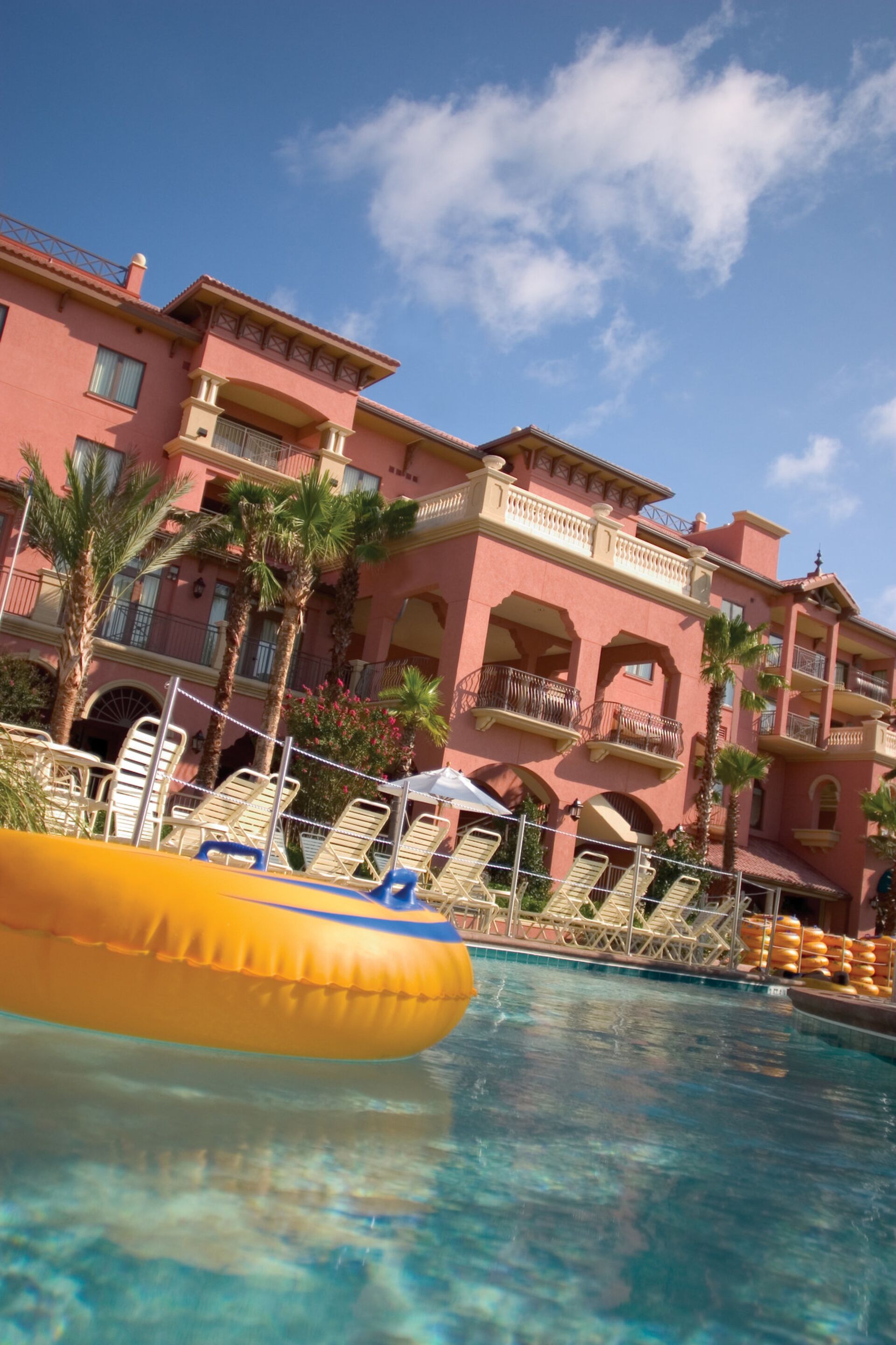 A hotel pool area with clear blue water, yellow inflatable float, and palm trees.