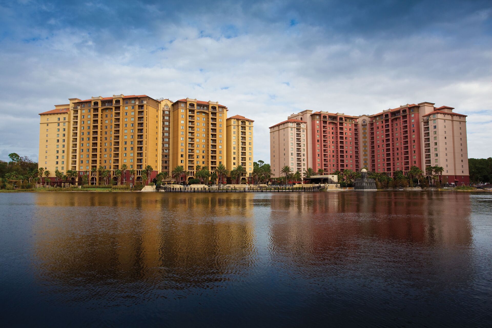 A high-rise hotel with multiple floors, a reflective water body in front, and a clear sky.