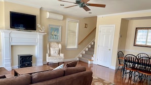 A living room with a brown sofa, a fireplace, a television, and a dining area with a table and chairs. - Cottage in Heart of Downtown Newport (Newport)